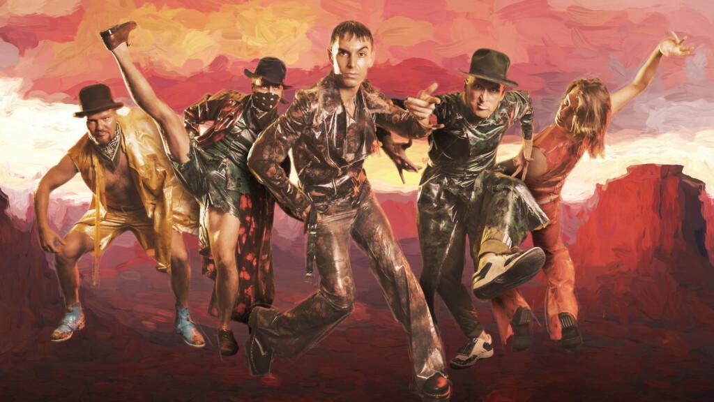 The dancers pose in their costumes in front of a wild west themed background.